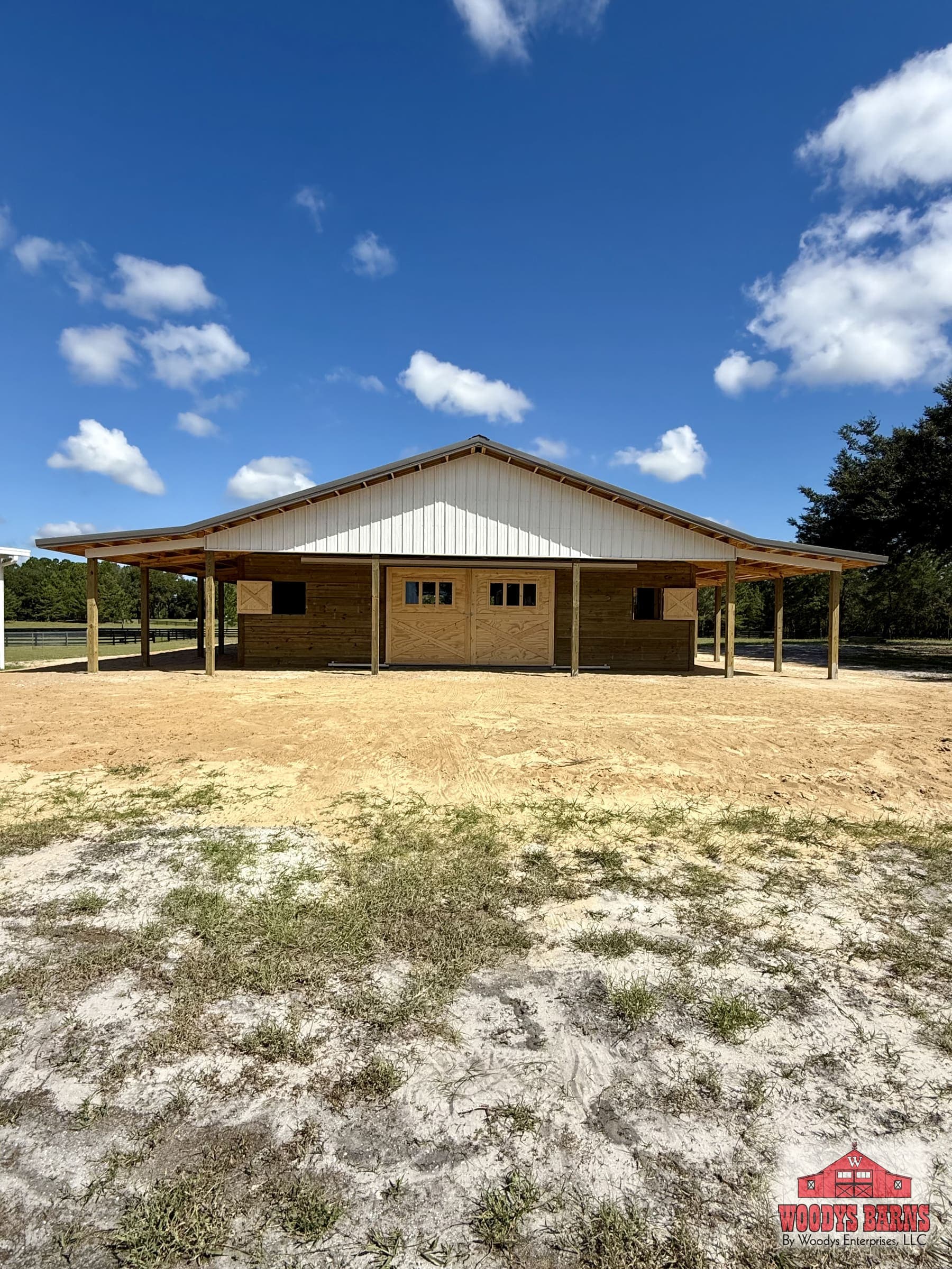 Custom center aisle horse barn with a charcoal grey metal roof, polar white gable and a wide covered breezeway, built by Woodys Barns in Florida